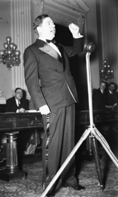 Long raises his fist as he speaks into a microphone