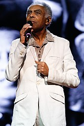 A man holding a microphone wearing a white suit
