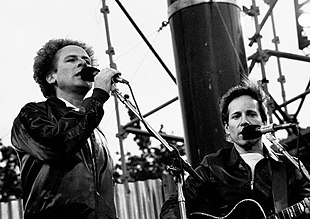 Two young men, one with blond hair and one with dark hair, singing into microphones on a stage