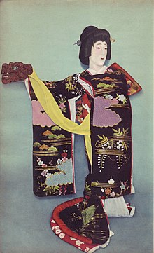 A colourised photograph of an actor in a long-sleeved, trailing kimono, wearing a traditionally-styled wig and holding a lion's head prop