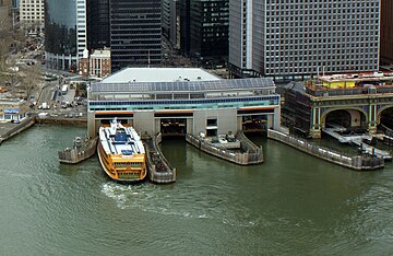 Three docks can be seen from the air, and next to them is a covered ferry terminal. This is an aerial view over a river.