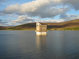 A lake with a pump house in the middle, surrounded by hills