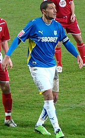 A footballer wearing a blue jersey and white shorts.