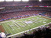 A view of a football field from the top of the stadium. The seats are about half empty. On the field is the marching band in a formation that spells out "HOKIES."