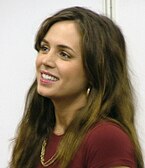 Eliza Dushku smiling at a convention in a maroon top