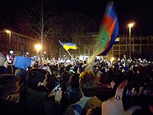 Hungarians demonstrate in Budapest at the onset of the Russian invasion of Ukraine in a public square at night, waving a Ukrainian flag