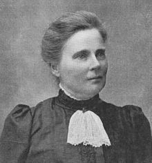 Portrait of a middle-aged white woman wearing a high-collared dark dress with a white lace tie at the neck.