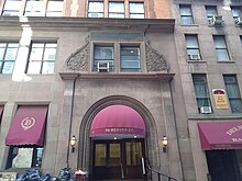 The building's entrance archway as seen from Beaver Street. The archway is recessed within a brownstone wall and has a red awning over it. There are windows above and to the left of the archway.