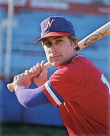 A man wearing a red baseball jersey and blue cap posed preparing to swing his bat