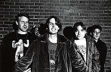 Pavement members standing before a brick wall posing in a black-and-white photo