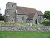 A flint church with a red tiled roof and a short west tower