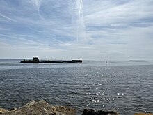 The Ballast bank in Wexford harbour. The photo shows a long, low stone structure in silhouette, set in the waters of a harbour.