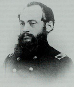 Photo shows a man with a dark, heavy beard. He wears a dark military uniform with two rows of buttons.