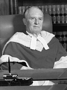 A white man sits in a black and white photo, wearing judicial robes and appearing approximately 50-60 years in age