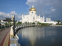 Large white mosque, with a gold dome, near water