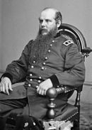 Black and white photo of a seated man in a dark military uniform with the shoulder tabs of a major general (two stars). He is balding and has a curly beard that reaches halfway to his waist.