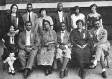 A group of six African-Americans, seven women and five men, posed for a group photo in two rows, six standing behind six seated.