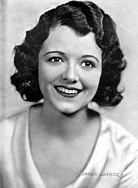 The image of a smiling Janet Gaynor. She is wearing a light-colored blouse.
