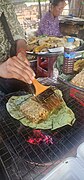 Cooking a grilled honeycomb with larvae at the Oudong Market in Cambodia