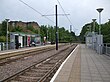 A set of two tram tracks between two platforms with shelters. Just before the horizon there is a level pedestrian crossing between the two platforms.