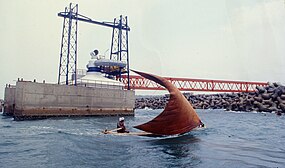 View from the sea of concrete caison with a turbine on top. A small boat is sailing in the foreground.