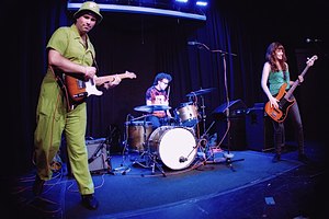 A guitarist, drummer, and bassist performing on a small stage