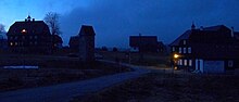 Polish town at dusk with no lights on except one at two houses.