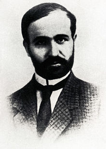 Black and white image of Skliros wearing a jacket and tie