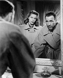 Lauren Bacall in black and white facing a mirror looking at Humphrey Bogart's reflection