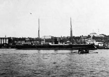 A black warship with two masts and a single funnel in port.