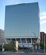 A glass office building slightly cantilevered over its base, giving it the appearance of being on stilts