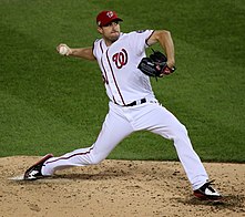 A man in a white baseball uniform with the Washington Nationals' red "W" on the front throws a pitch.