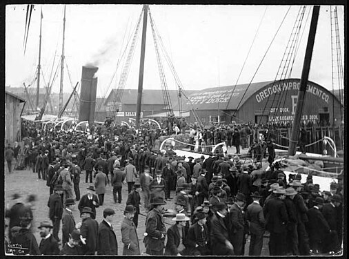 The steamship Australia at Pier B, circa 1898. I'm 99% certain that the people in the foreground here are on Pier A (which the 1893 map shows as longer than Pier B) and that we are seeing the same end of the dock as in the pictures that are clearly either from the water or from the far longer King Street Coal Pier. Note that at this time Lilly Bogardus appears to have one, or just possibly two, of the three transverse structures shown in the circa 1900 photos. You can see a sign saying "Lilly" just west of center, and some mostly illegible writing on the roof ending in "City Dock". Written on end of pier shed: "Oregon Improvement Co.", "City Dock", a big "B", and what appears to be the same smaller writing about Lilly Bogardus as in the circa 1900 photos: "Lilly Bogardus Co.'s Dock / Hay, Grain, Flour and Seed".