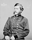 Black and white photo shows a man with a moustache and mutton chop sideburns. He wears a dark military uniform with two rows of buttons and the shoulder tabs of a major general.