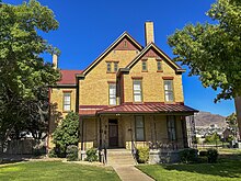 A tan brick two-story house in Queen Anne-style architecture is shown from the front side.