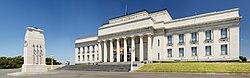 Large neoclassical-style building with a forecourt featuring a Cenotaph on a Court of Honour. Above the front porch of the building is inscribed a funeral oration attributed to the Greek General Pericles, which reads "MCMXIV – MCMXVIII / The whole earth is the sepulchre of famous men / They are commemorated not only by columns and inscriptions in their own country / but in foreign lands also; by memorials graven not on stone / but on the hearts of men." A New Zealand flag atop the building is flown at half-mast. Banners hanging between the columns advertise exhibitions about volcanoes, and Charles Darwin.