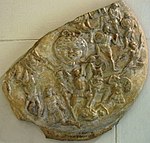 fragment d'un objet rond décoré d'une scène de combat avec une tête grotesque au centre
