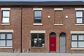 A colour photo of a red-bricked house with boarded up windows and doors