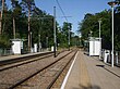 A set of two tram tracks between two platforms with shelters.