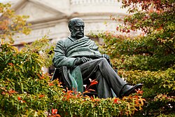 A statue of a seated man surrounded by trees leaves and branches