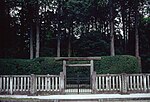 Concrete fence and torii in front of a hedge and trees.