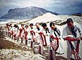 Photograph of a 1942 memorial service at Kaneohe Naval Air Station, showing sailors placing leis on graves of men killed during the Pearl Harbor Attack.