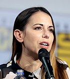 An adult American woman with long brown hair speaking into a microphone.