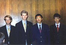 Four boys, in their late teens, wearing shirts, ties and blazers, standing in a line. The two on the left are white, while the two on the right are of oriental origin