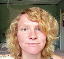 A white woman with wavy blond hair seen from the chin up against a green background
