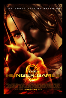 The poster shows Katniss Everdeen aiming a bow with an arrow. The tagline on top reads "The World Will Be Watching". Behind the film's titles, a golden Mockingjay pin with the Mockingjay carrying a bow in its beak and flames surrounding it. The credits and release date are labeled below the film title.