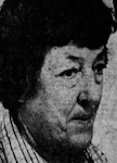 An older white woman with dark hair, wearing a plaid collared shirt.