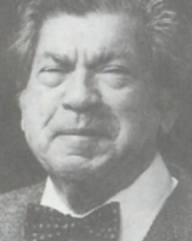 headshot of an older man with squinty eyes and bushy hair wearing a bowtie and a suit jacket