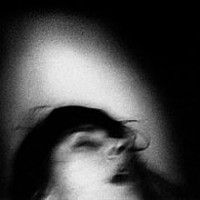 A blurry black and white photograph of a person's face. The person occupies the lower portion of the photo facing upwards. Their eyes are closed and their mouth is slightly open.