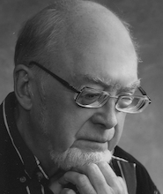 black and white tight headshot of an older man with glasses, staring down with his head in his hand.